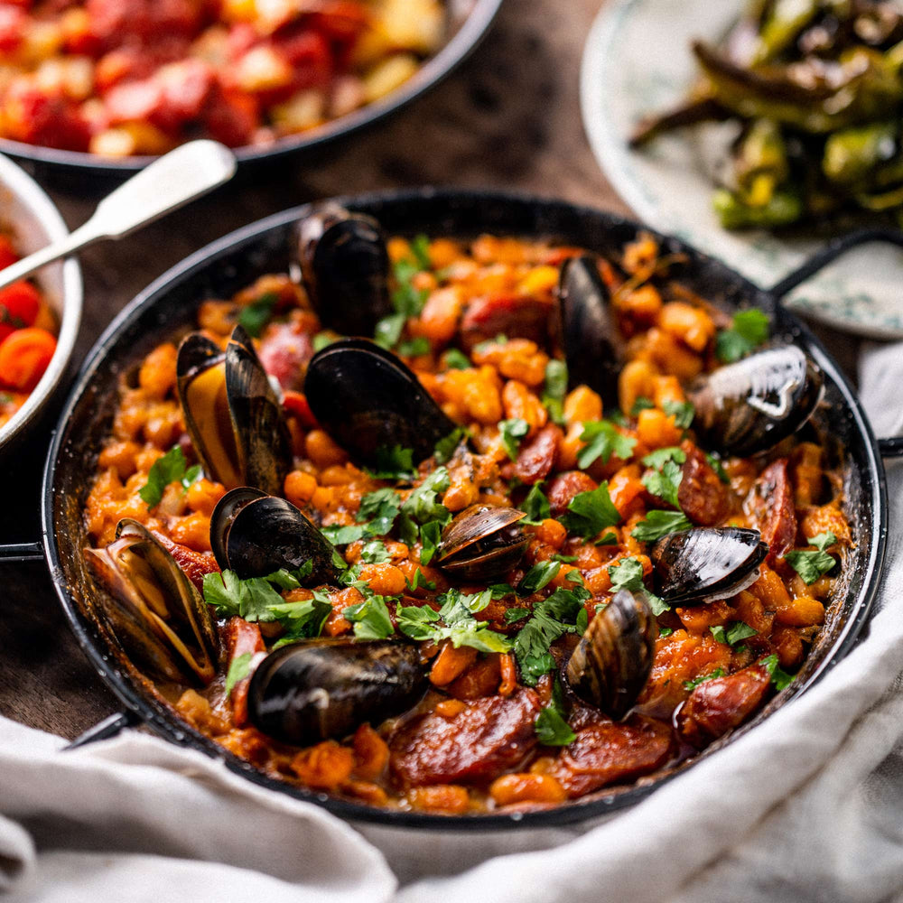 Artistic shot of baked chorizo, mussels and butter beans on a serving plate ready to eat.