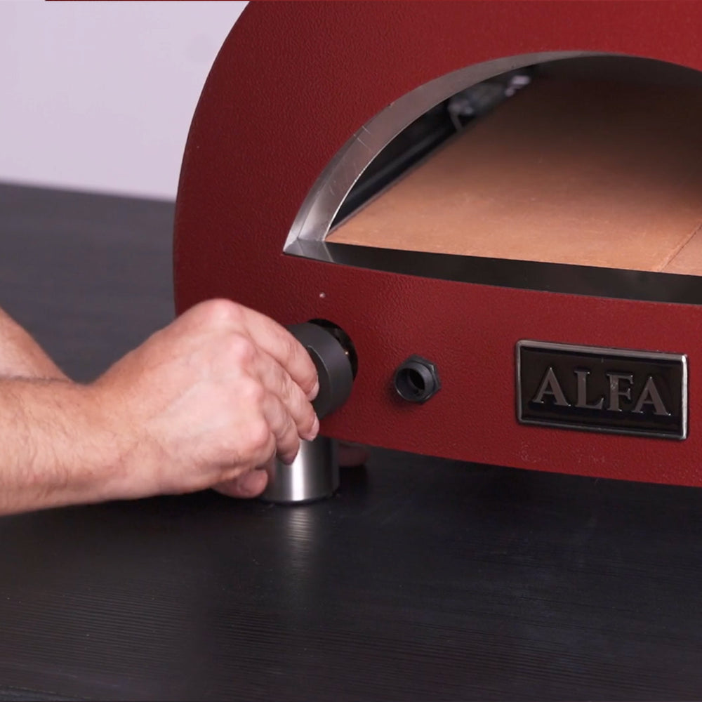Close up of a mans hand turning the dial of a red alfa portable oven.