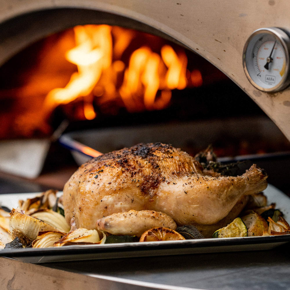 Close up of a roast chicken with vegetables in a tray sitting in front of an alfa oven.
